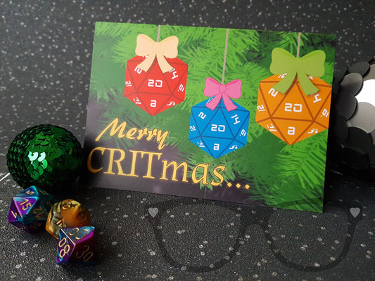 Christmas card for geeks showing a red, yellow and blue 20 sided dice hanging from a Christmas tree, the text reads "Merry CRITmas"