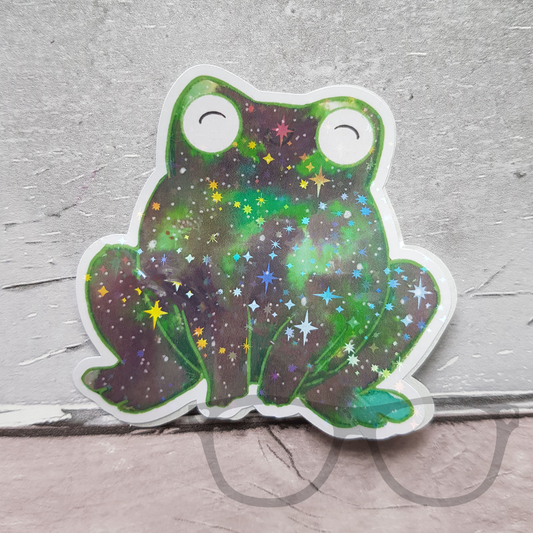 Frog sticker with a green nebula and sparkle overlay, cosmic design on vinyl.