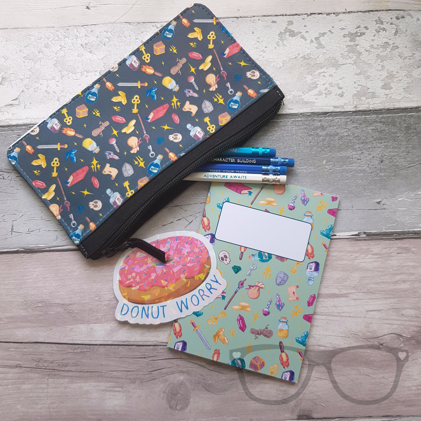 Zipped pencil case for school, college or university featuring a Fantasy genre pattern on a teal background. Shown with a range of stationery including pencils, a notebook and a sparkly donut sticker that reads "Donut Worry"