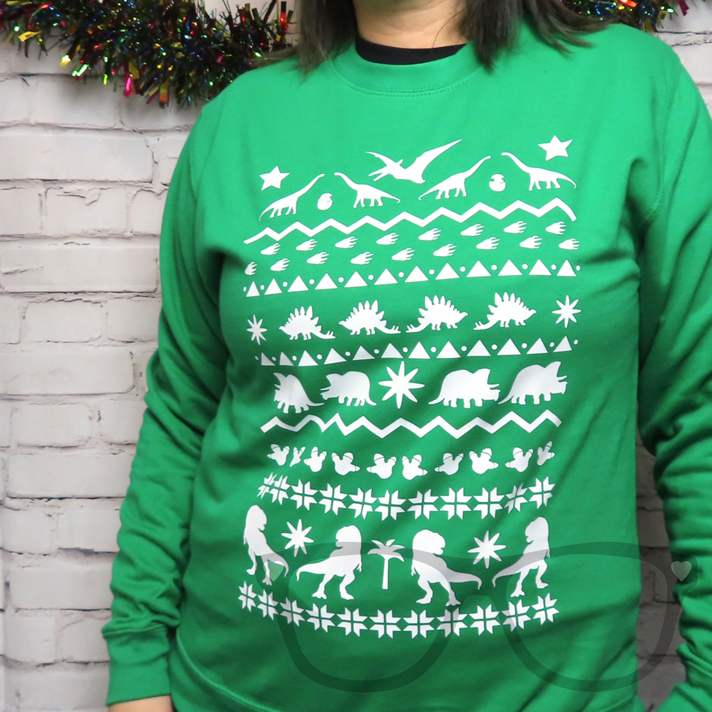 A Green sweater being worn to show the full design of the rows of dinosaurs and shapes to mimic a Christmas sweater design