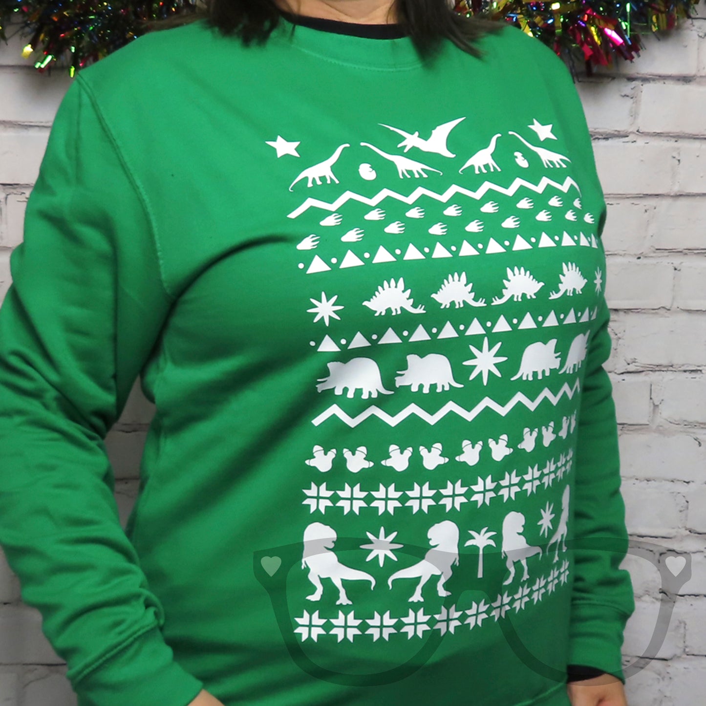 A three quarter view showing the green dinosaur sweater being worn.  The full length white design shows rows of dinosaurs, shapes and dino footprints . Ideal for winter, festive celebrations