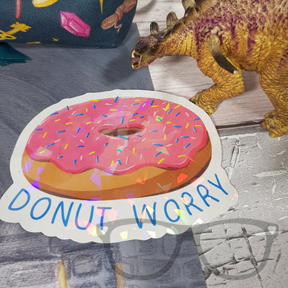 Donut Worry sparkling vinyl sticker placed alongside Derek the Dinosaur sticker, ideal for adding fun to your belongings.
