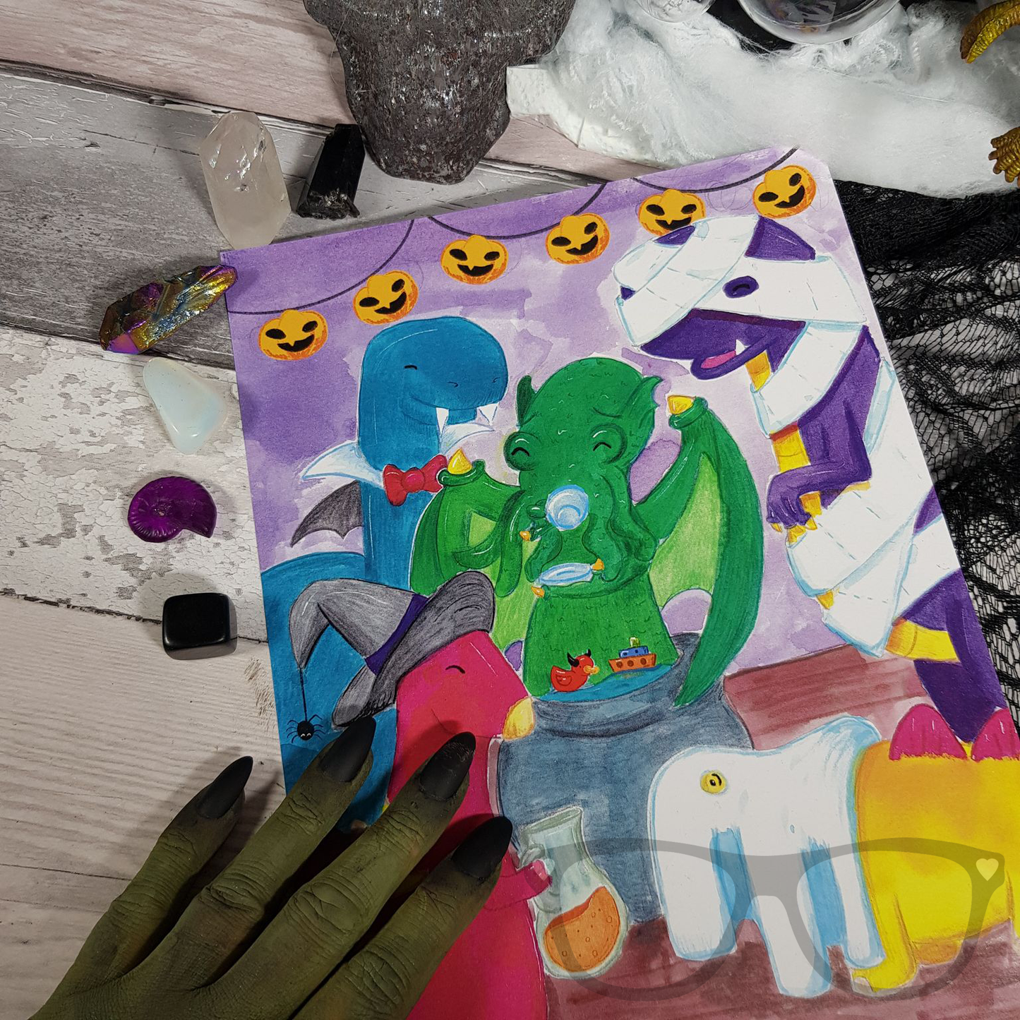 A witches hand holding the A4 artprint of the dinosaurs enjoying the spooky Halloween Party