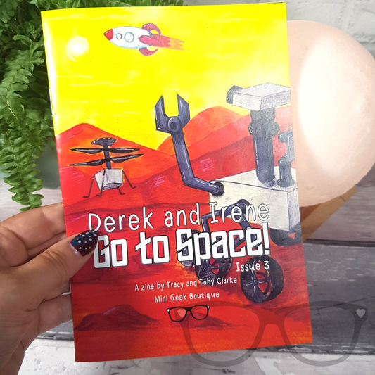 Issue 3 of the Derek and Irene zine being held, featuring a colourful space adventure theme with a rocket and space-themed illustrations