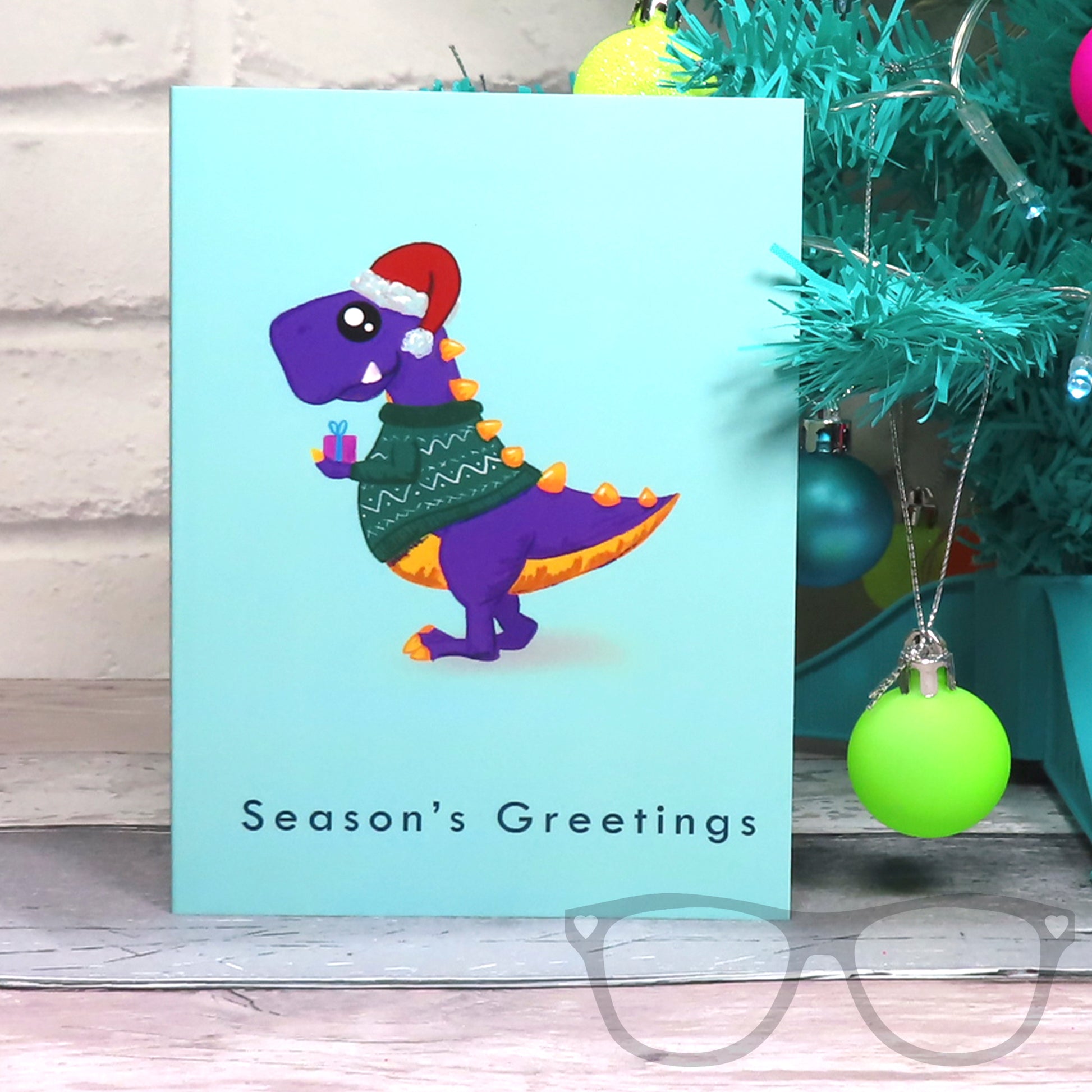 Green Christmas Card featuring a t.rex holding a gift and wearing a festive jumper