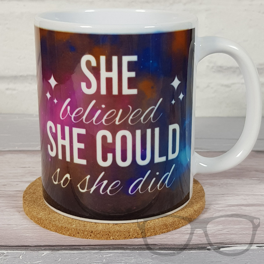 She believed she could so she did on a white ceramic straight sided 11oz mug. The design shows a multi coloured space background with white text that reads "She believed she could so she did"
