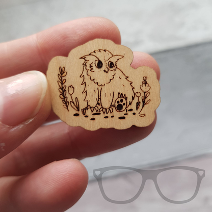 Wooden Owlbear pin being held to show scale